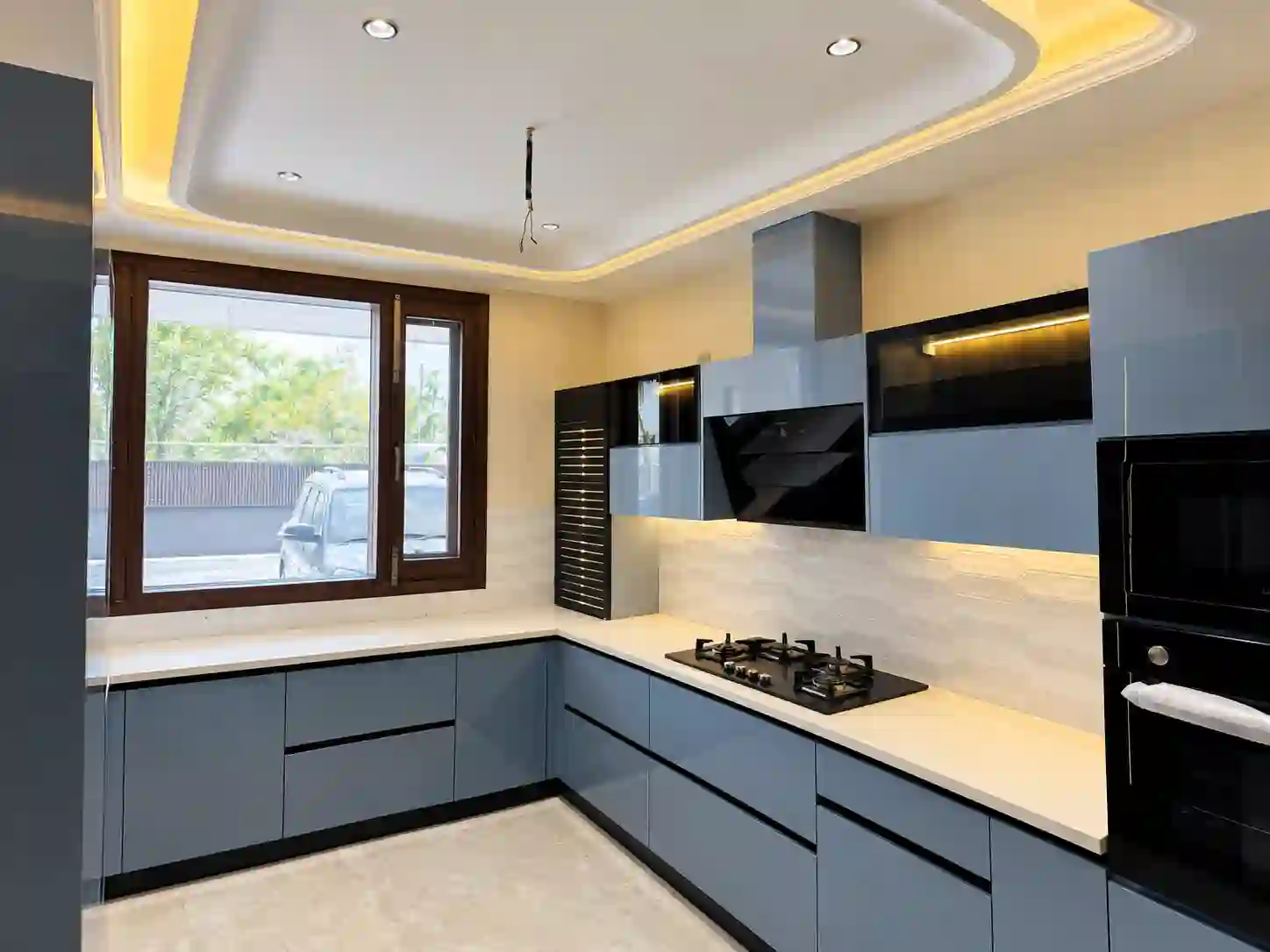 Blue L-shaped modular kitchen with integrated appliances and a large window