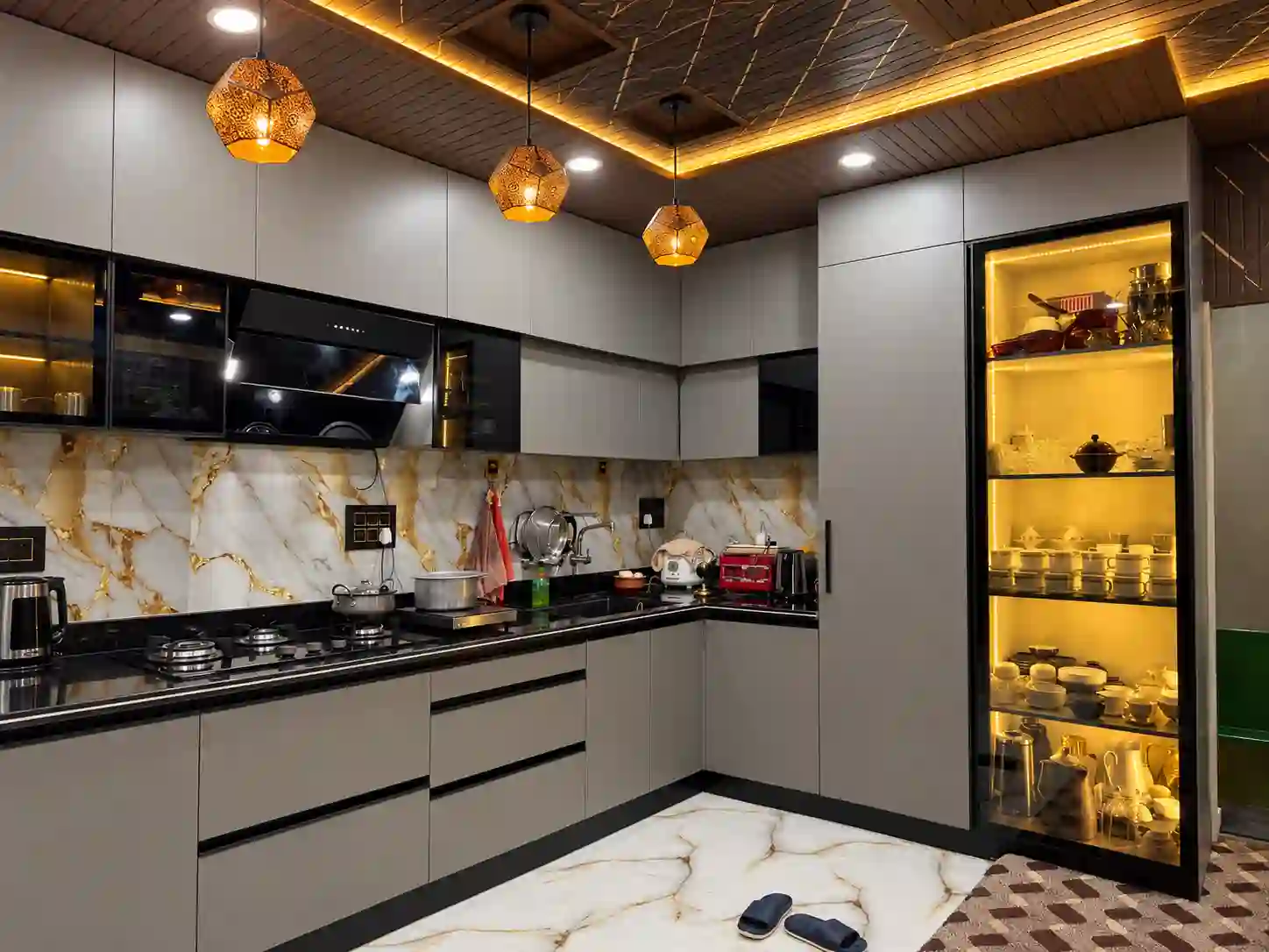 Grey and white L-shaped modular kitchen with marble-effect backsplash and illuminated display cabinet